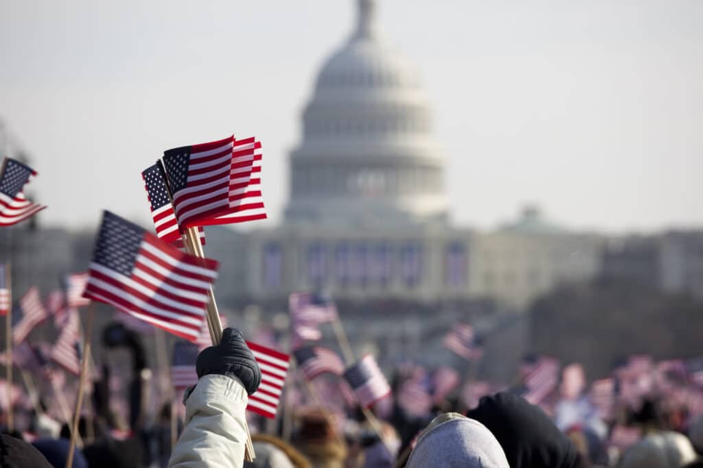 Unrecognizable crowds in the Washington DC Mall. Several American flags are being held up in the air.