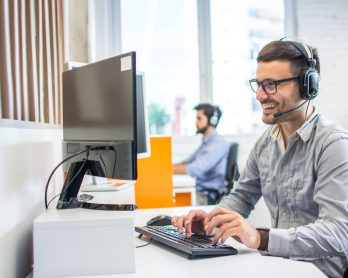 Friendly service agent using computer and talking to customer in call centre